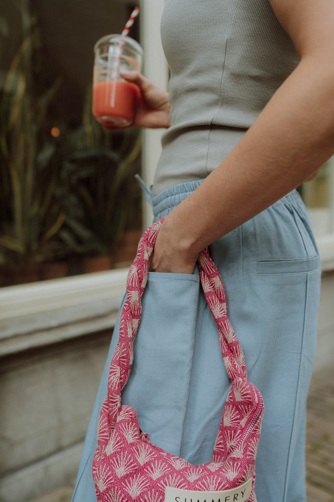 Woman wearing blue pants holding pink patterned bag in street style outfit.