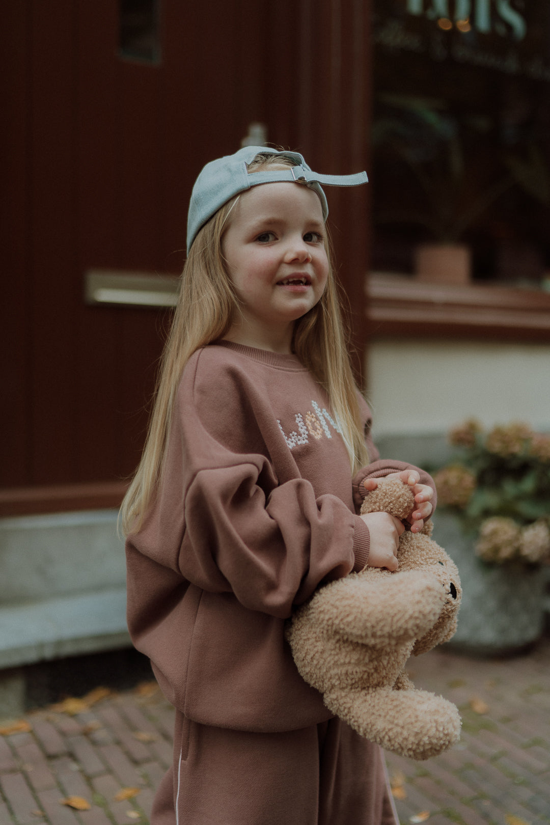 Young girl wearing a mauve lounge set and blue cap.
