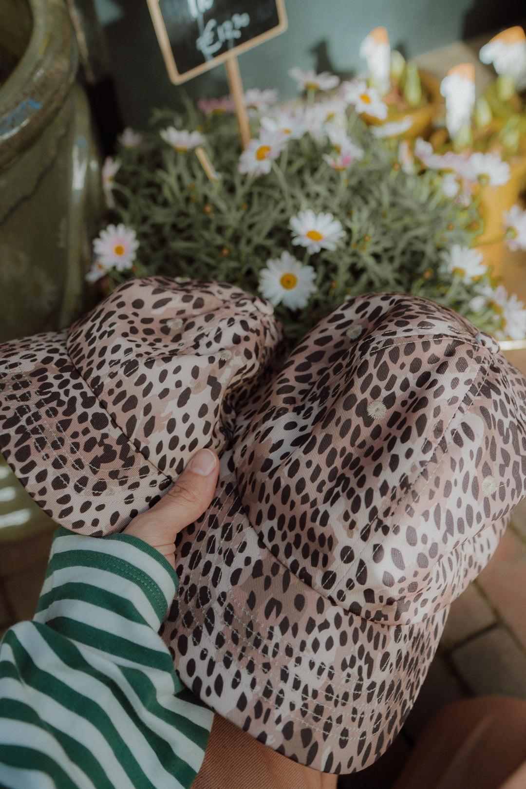 Close-up of a leopard print kids bucket hat held by hand with flowers in the background