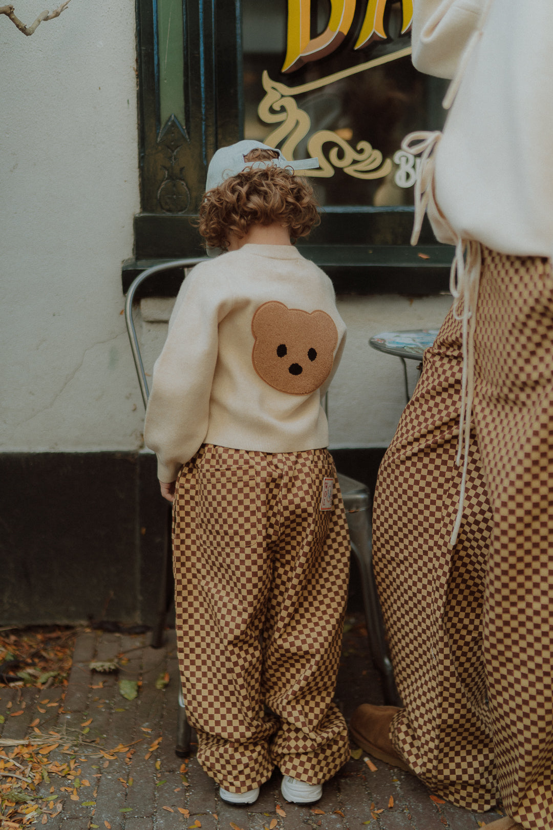 Child wearing checker pants and a cream knit sweater with a teddy bear