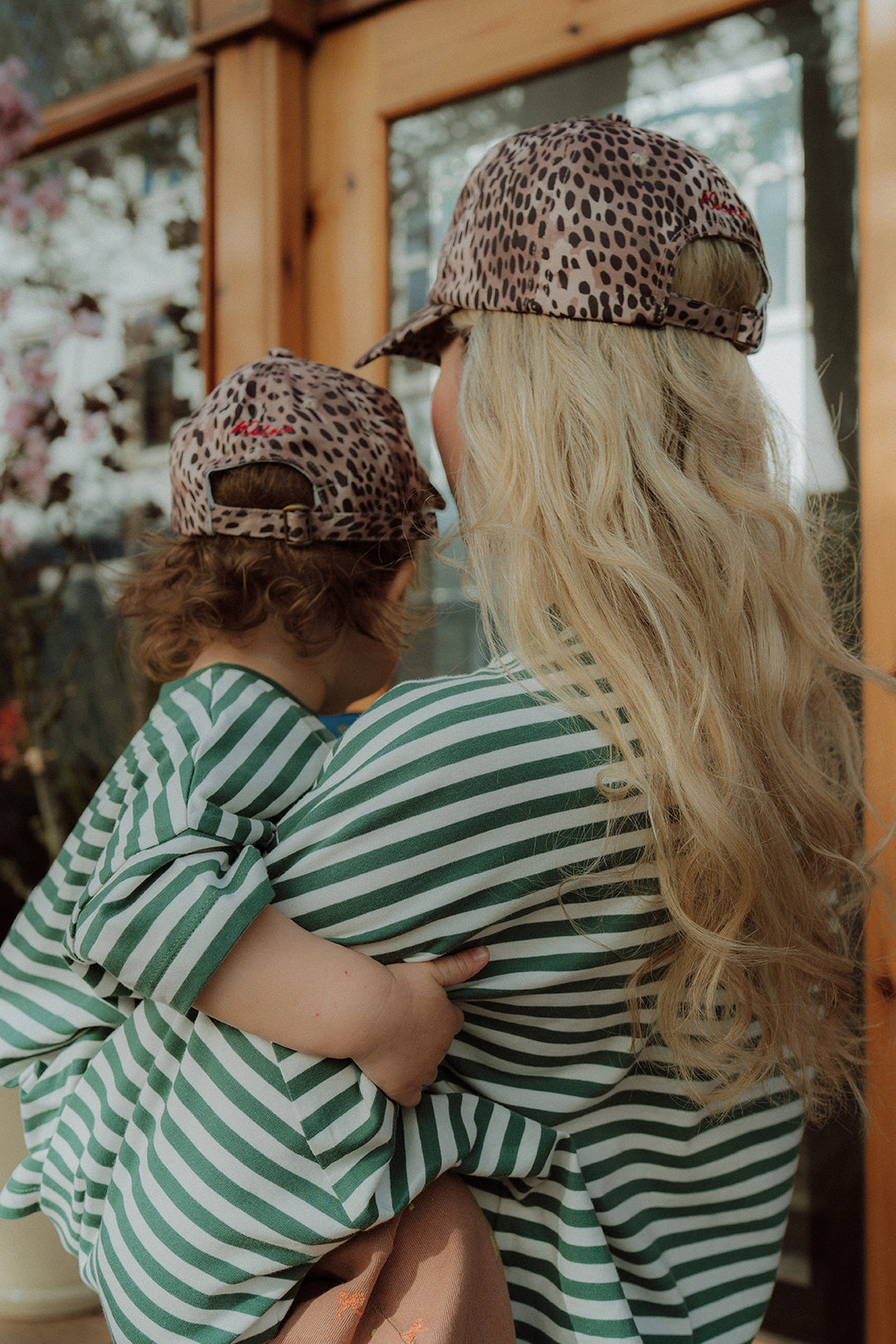 Back view of mom and toddler in matching green striped outfits with leopard caps