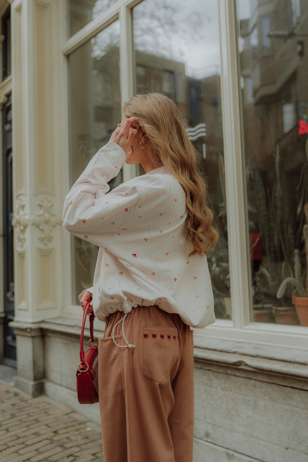 Woman wearing a cream embroidered WOLVIE sweater with loose brown pants walking outdoors.