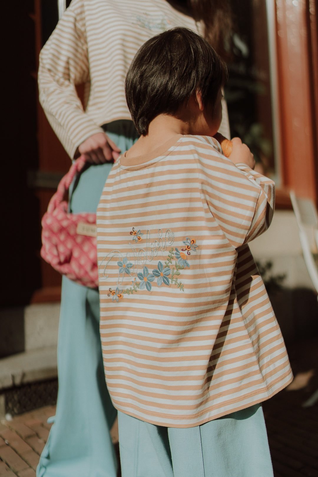 Young child wearing a striped WOLVIE shirt with floral back print and loose blue pants outdoors
