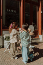 Two children wearing striped oversized shirts and wide leg pants outside a cafe