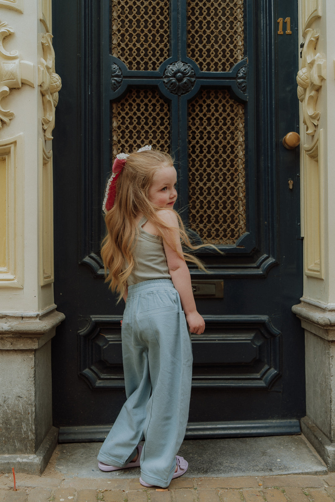 Girl wearing blue pants and sleeveless top standing in front of a door in street style outfit.