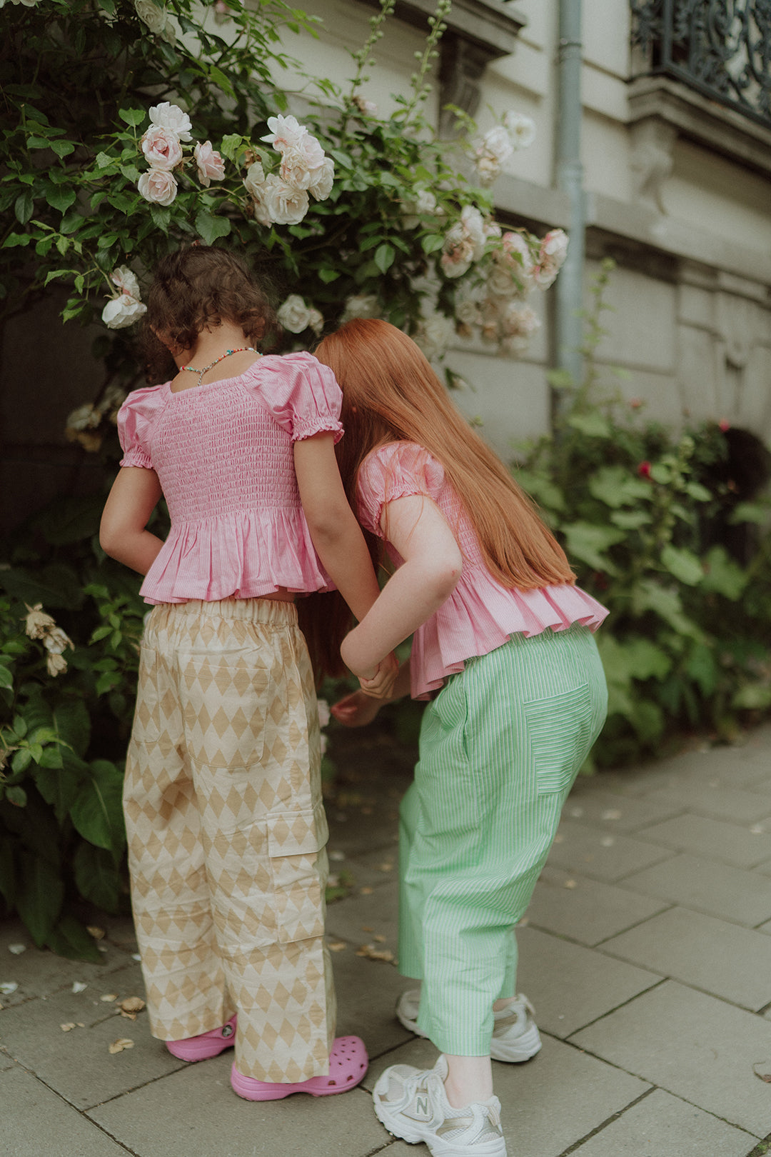 Two girls wearing pink smocked tops with patterned and green striped pants