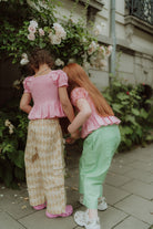 Two girls wearing pink smocked tops with patterned and green striped pants