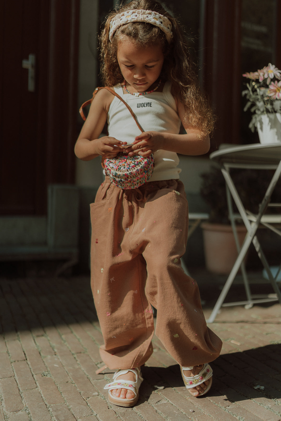Girl wearing a summer outfit with wide leg pants, a white top and colorful crossbody bag