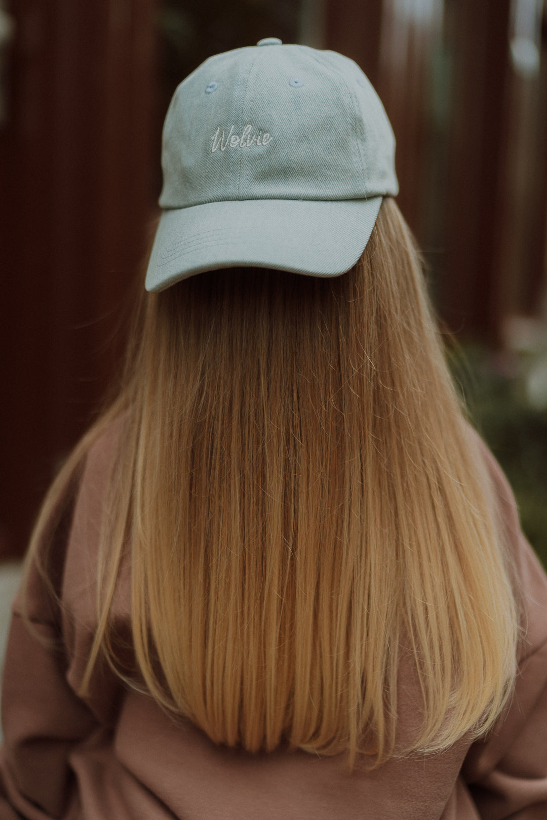 Back view of a child wearing a light blue logo cap and sweatshirt outdoors.