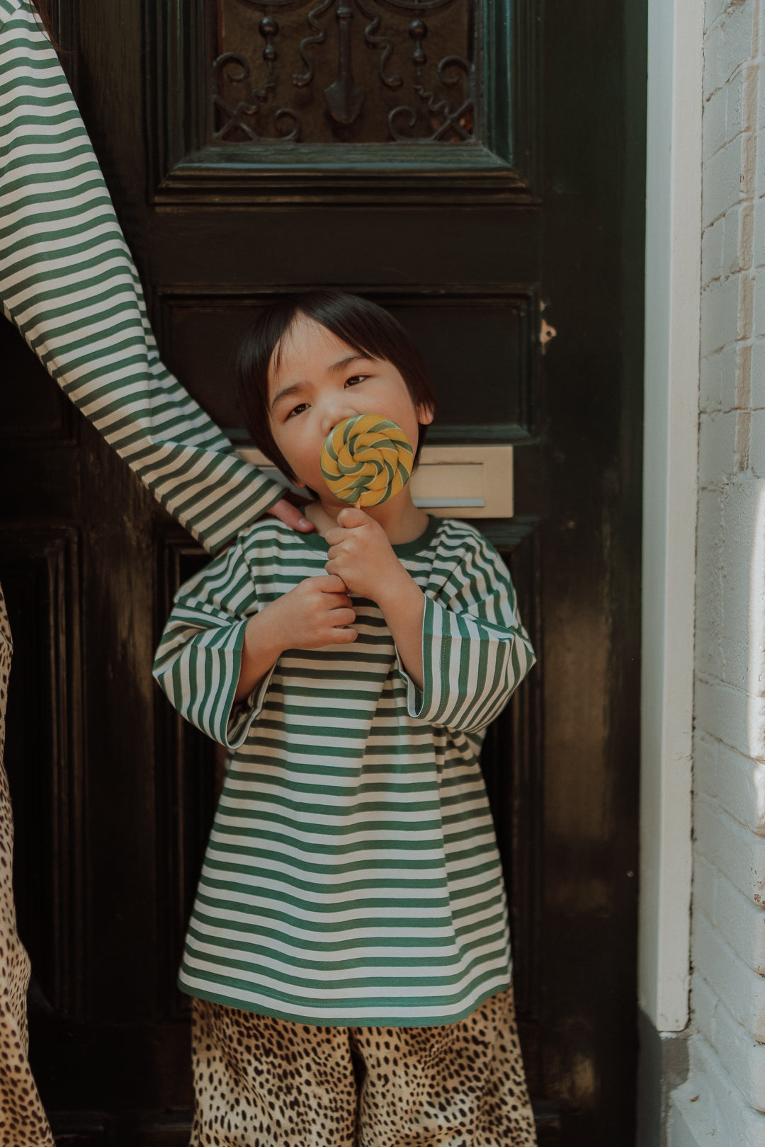 Kid wearing a green striped oversized top with leopard print pants as a matching outfit