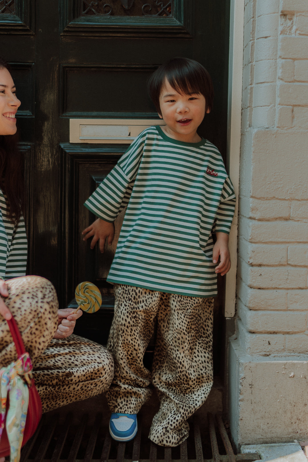 Child wearing striped shirt and leopard pants outfit by Wolvie standing in front of a door