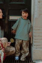 Child wearing striped shirt and leopard pants outfit by Wolvie standing in front of a door