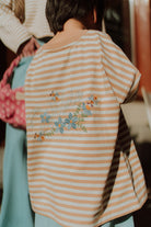 Child wearing oversized beige striped shirt with floral print detail on the back