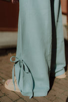 Close-up detail of light blue wide leg pants with tie accents at the bottom