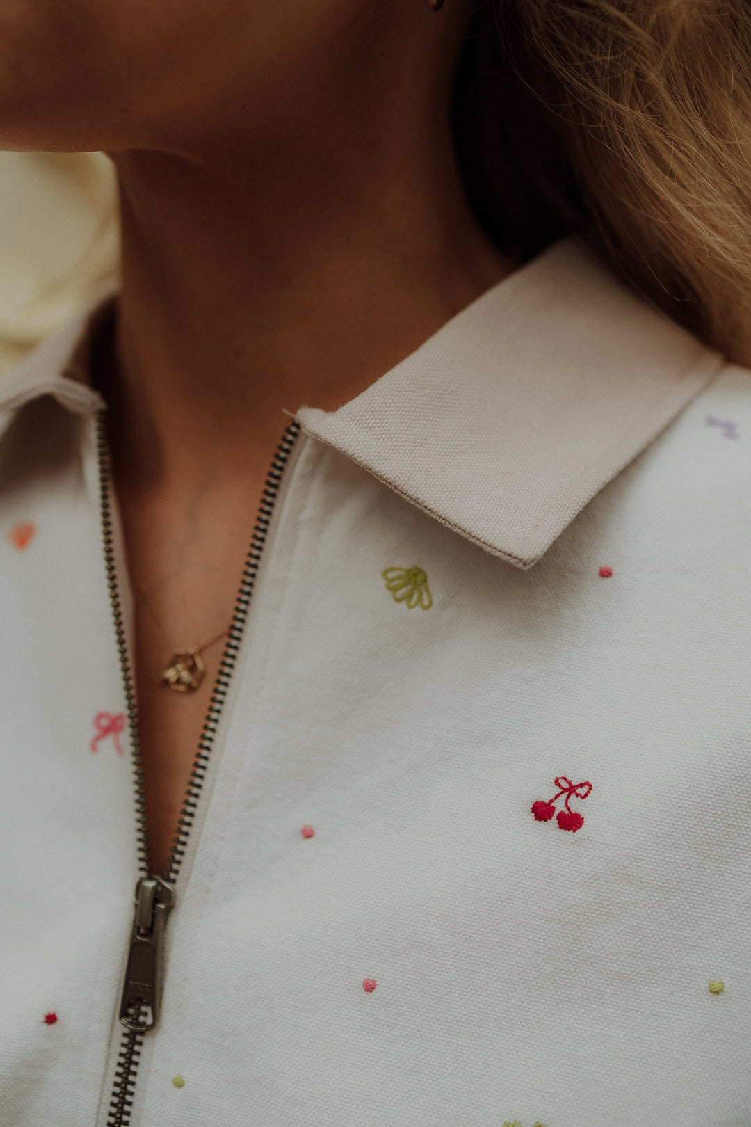Close-up of cream matching clothes sweater with zipper detail and embroidered colorful accents for women and moms