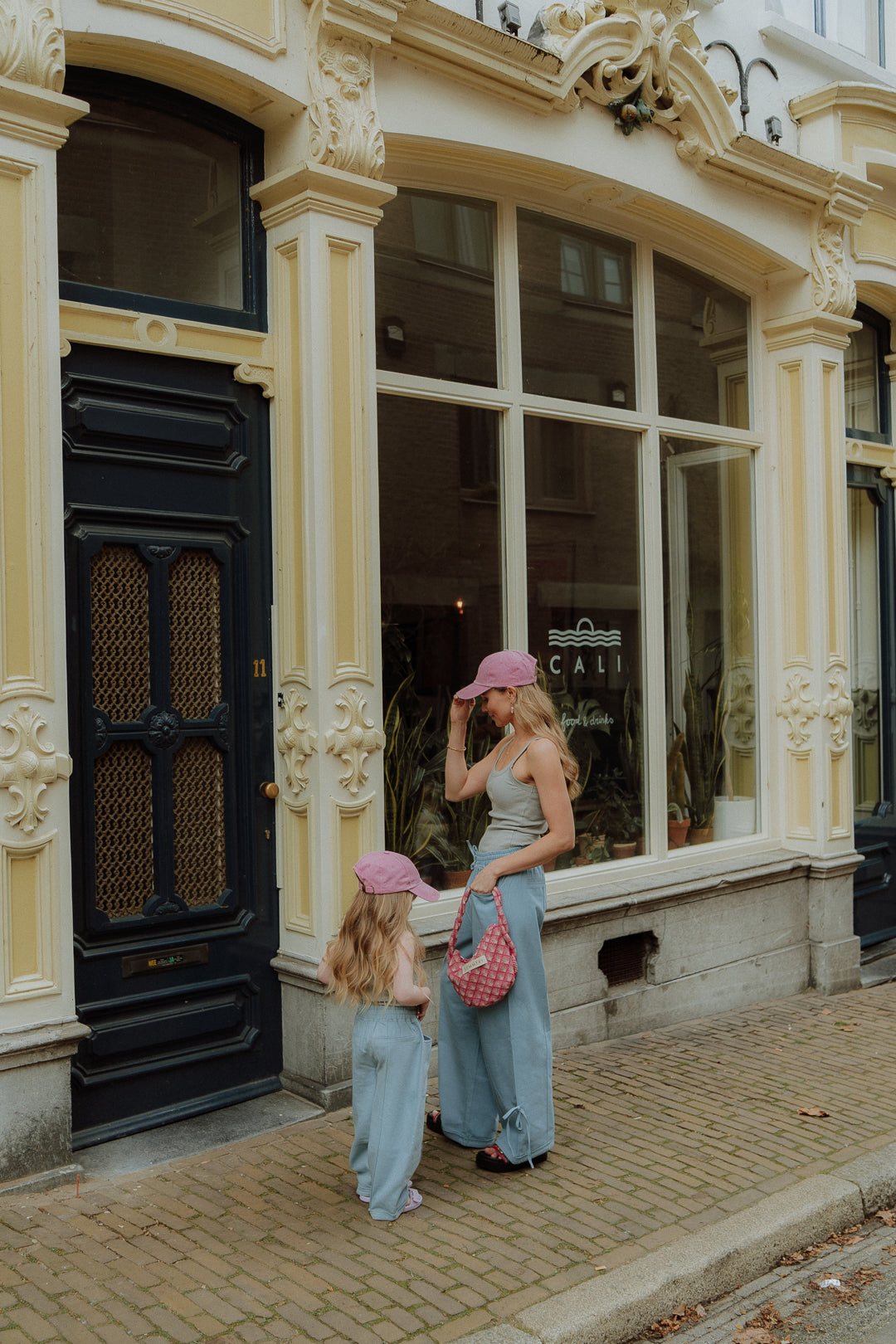 Mother and child wearing matching mom and child outfit with green pants and sleeveless tops standing on a street.