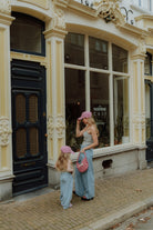 Mother and child wearing matching mom and child outfit with green pants and sleeveless tops standing on a street.