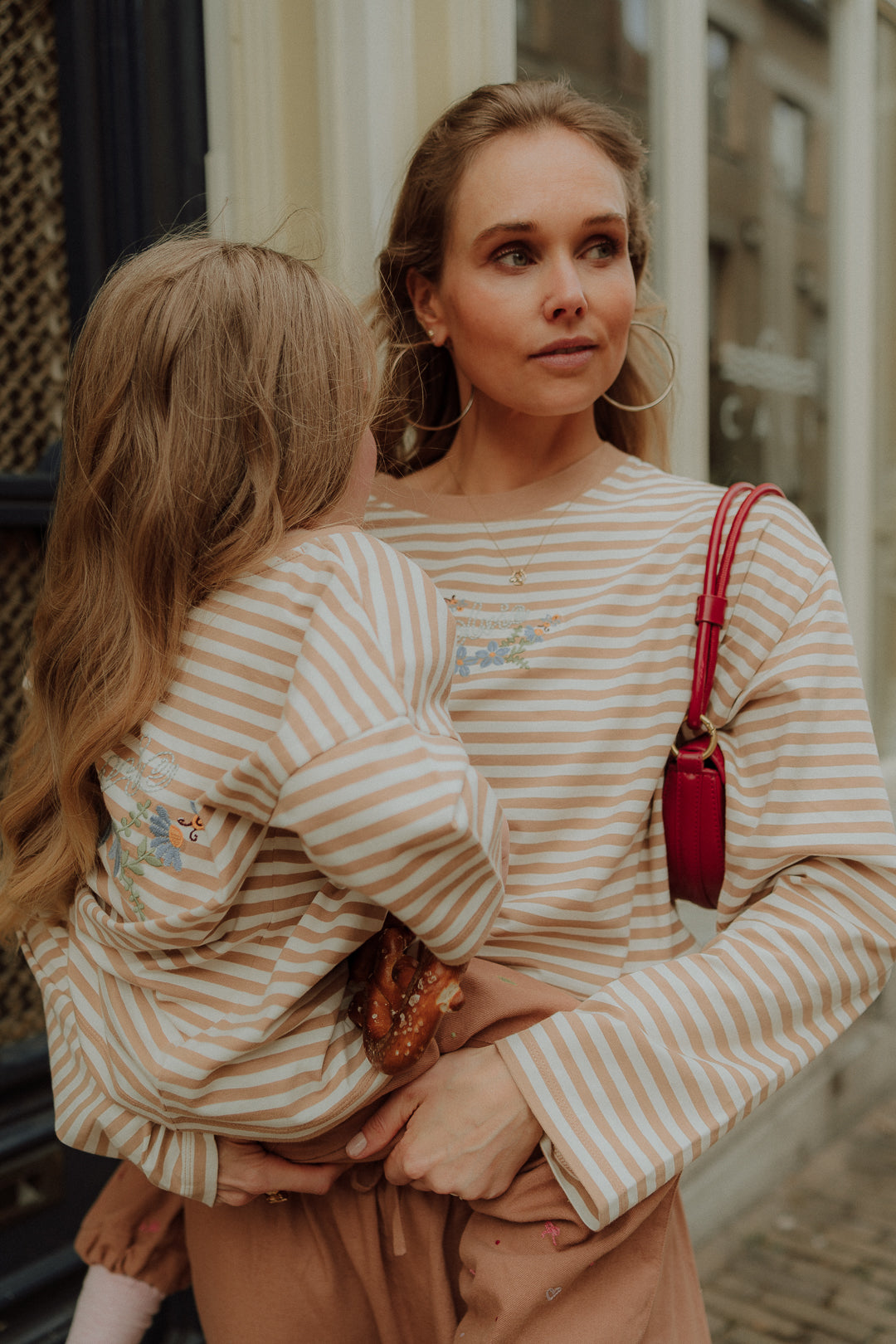 Matching mom and daughter striped outfit beige tones holding child street style.