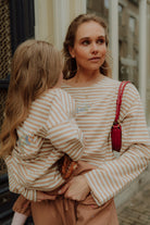 Matching mom and daughter striped outfit beige tones holding child street style.