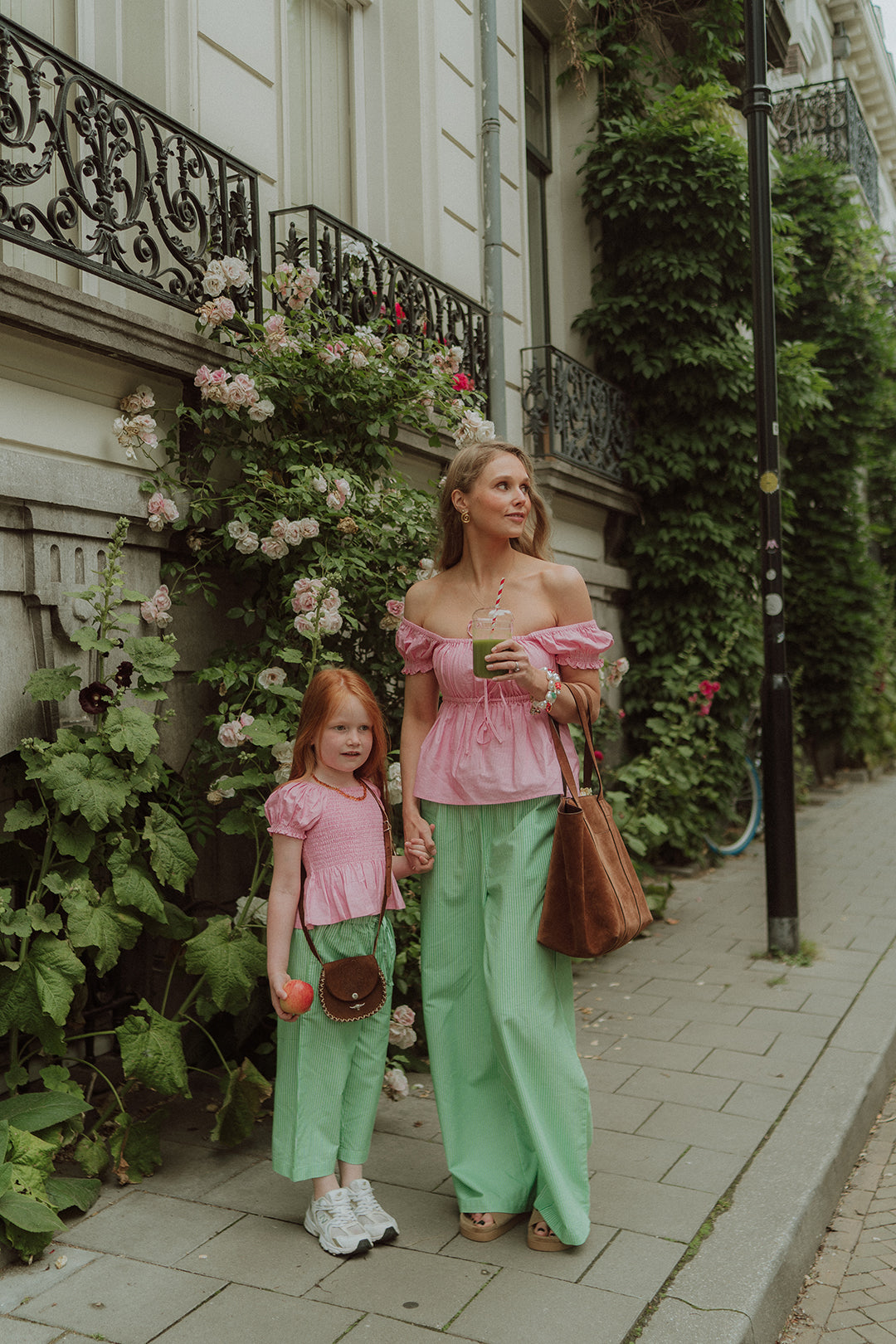 Mother and daughter wearing matching pink tops and green striped pants while standing