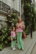 Mother and daughter wearing matching pink tops and green striped pants while standing