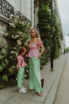 Mother and daughter wearing matching pink tops and green striped pants.