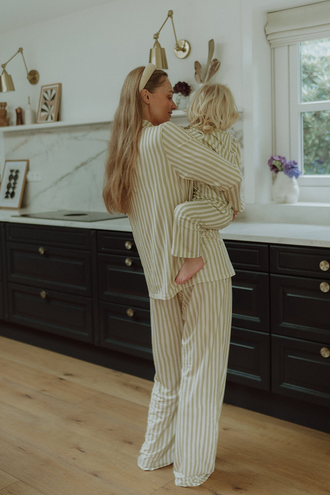 Mother holding child while wearing matching beige striped pajamas