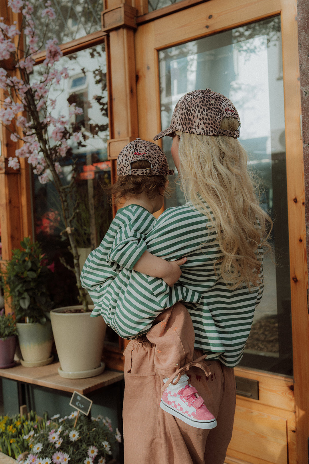 Mom and toddler in matching green striped outfits with leopard print cap outside flower shop