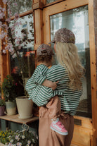 Mom and toddler in matching green striped outfits with leopard print cap outside flower shop