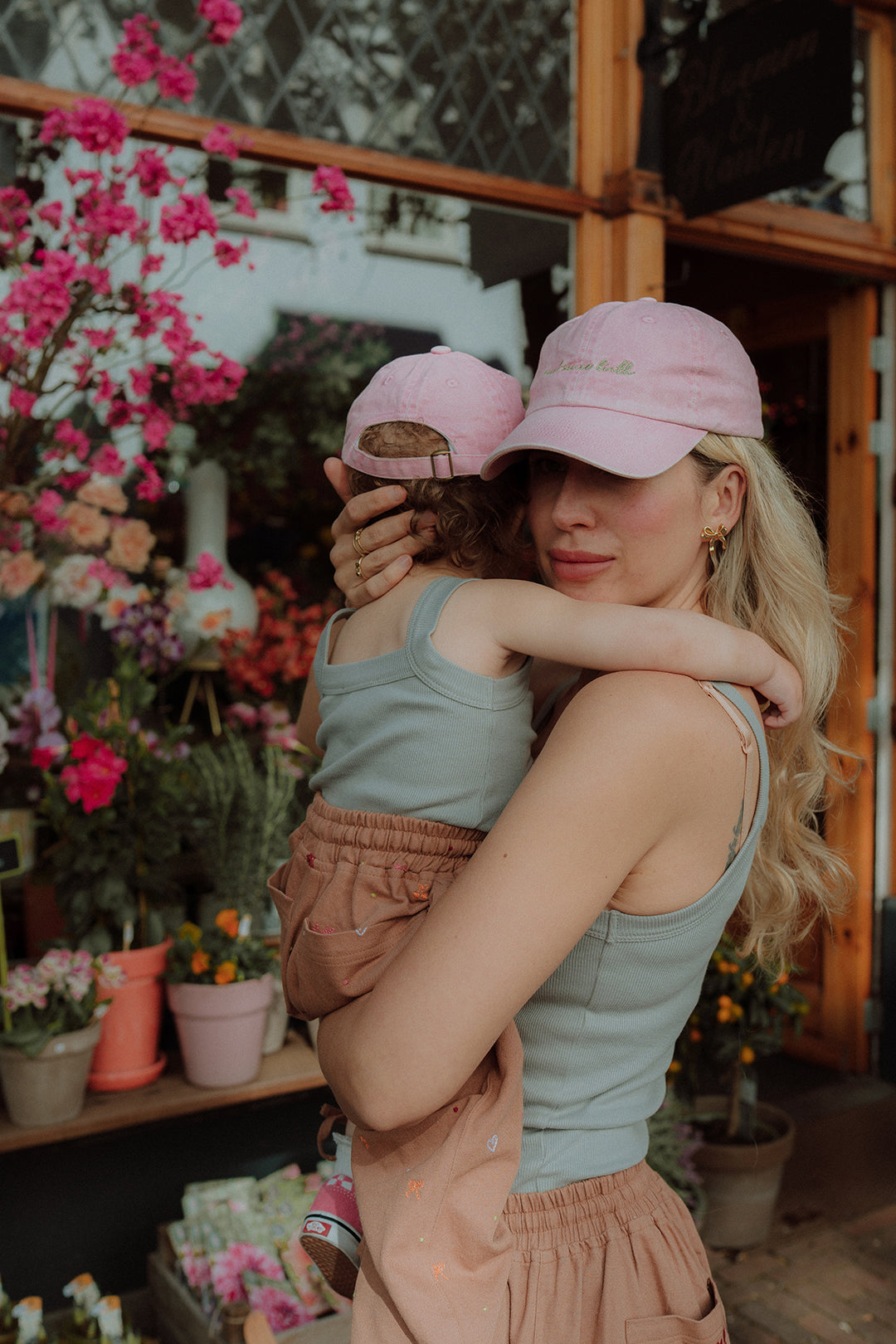 Mom and toddler in matching outfit with pink caps hugging outside flower shop