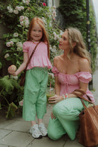 Mother and daughter wearing matching pink tops and green striped pants in a floral street setting.