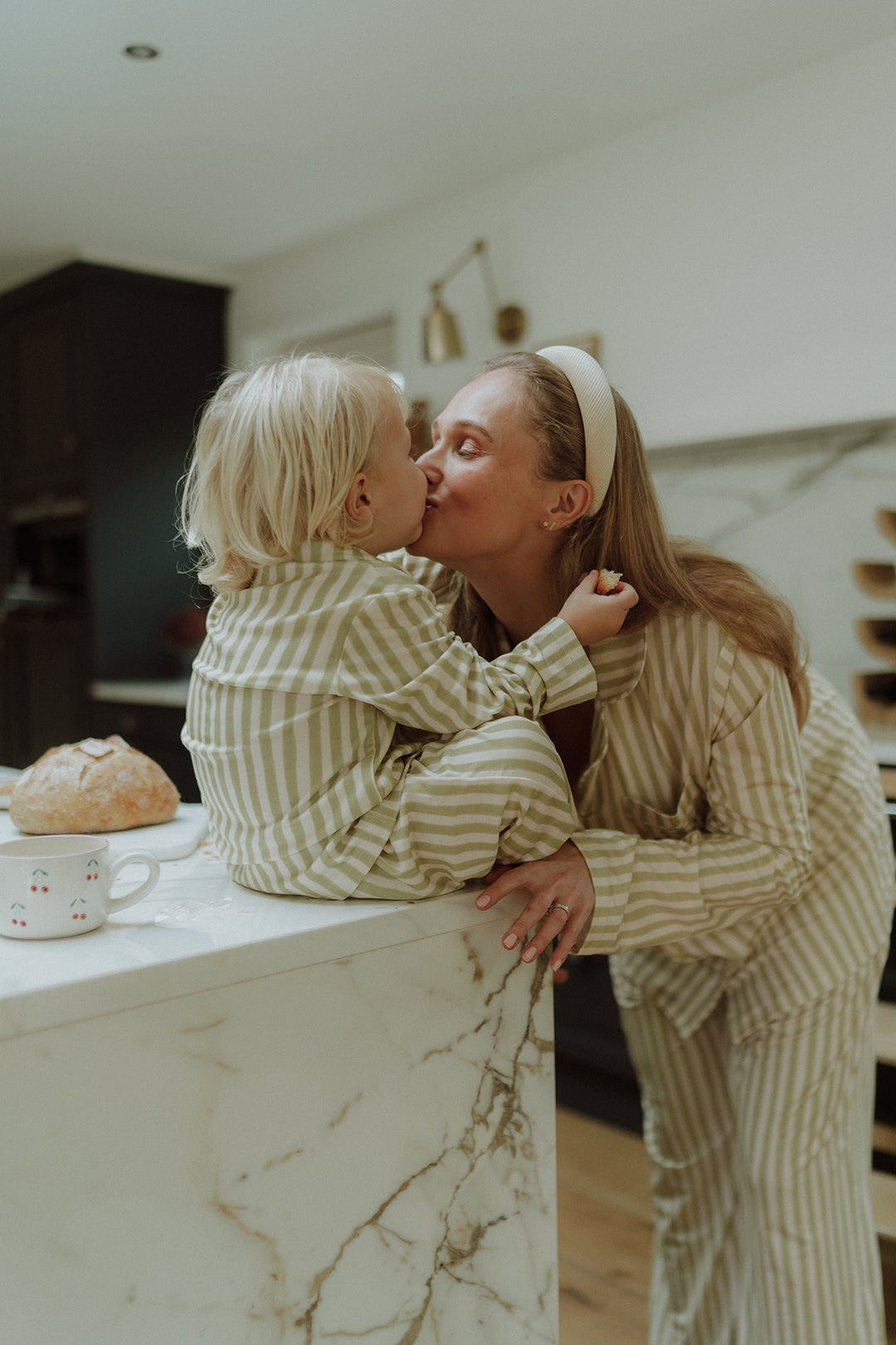 Mother kissing child while wearing matching beige striped pajamas 