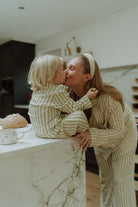 Mother kissing child while wearing matching beige striped pajamas 
