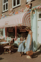 Mother and daughter wearing matching light blue summer dresses outside a pastel café in a stylish mommy and me fashion look
