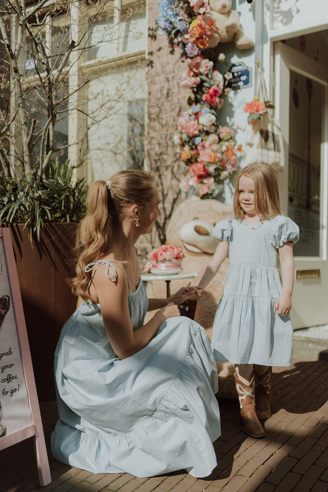 Mother and daughter wearing matching light blue dresses in a dreamy summer setting with floral decorations and soft pastel tones