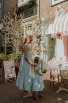 Mother and daughter wearing matching light blue dresses outside a pastel café with floral decorations and a soft dreamy summer aesthetic