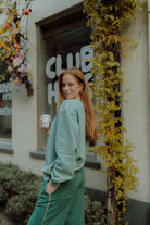 Woman wearing an oversized green sweatshirt and matching sweatpants outdoors. Neutral women loungewear by Wolvie