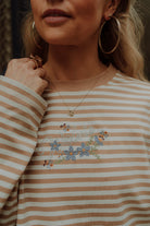 Close-up of beige striped long sleeve shirt with embroidered floral logo for women