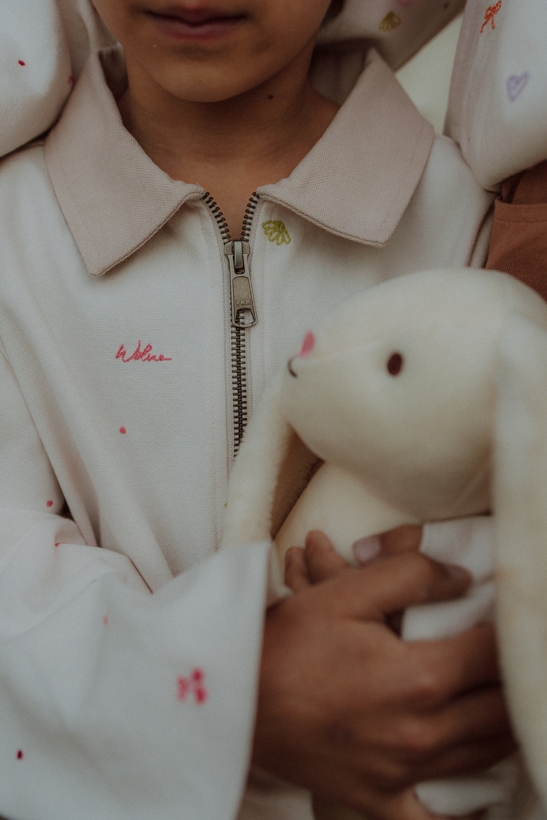 Child wearing light beige embroidery jacket from Wolvie SS26 collection holding a plush toy