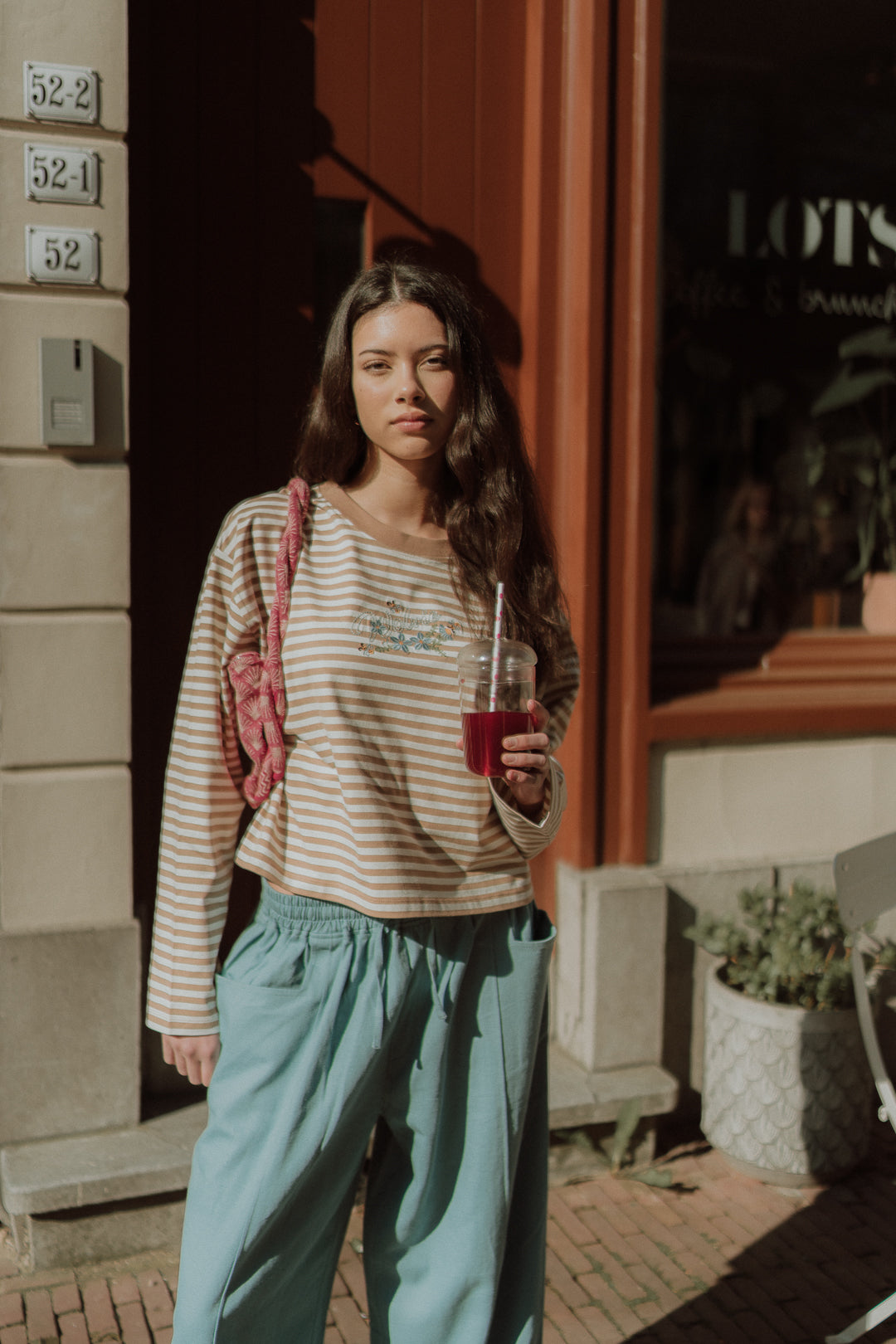 Woman wearing a striped WOLVIE top with relaxed blue pants while holding a drink outdoors.