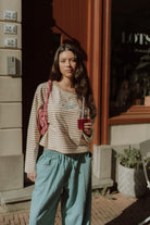 Woman wearing a striped WOLVIE top with relaxed blue pants while holding a drink outdoors.