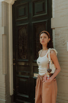 Woman wearing a neutral WOLVIE summer outfit with a white ruffle top and relaxed brown pants