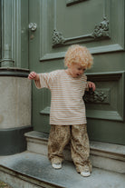 Toddler wearing matching mom and child outfit with striped shirt and leopard print pants standing by a green door.