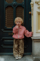 Toddler wearing red gingham jacket and leopard print pants standing in front of a dark blue door
