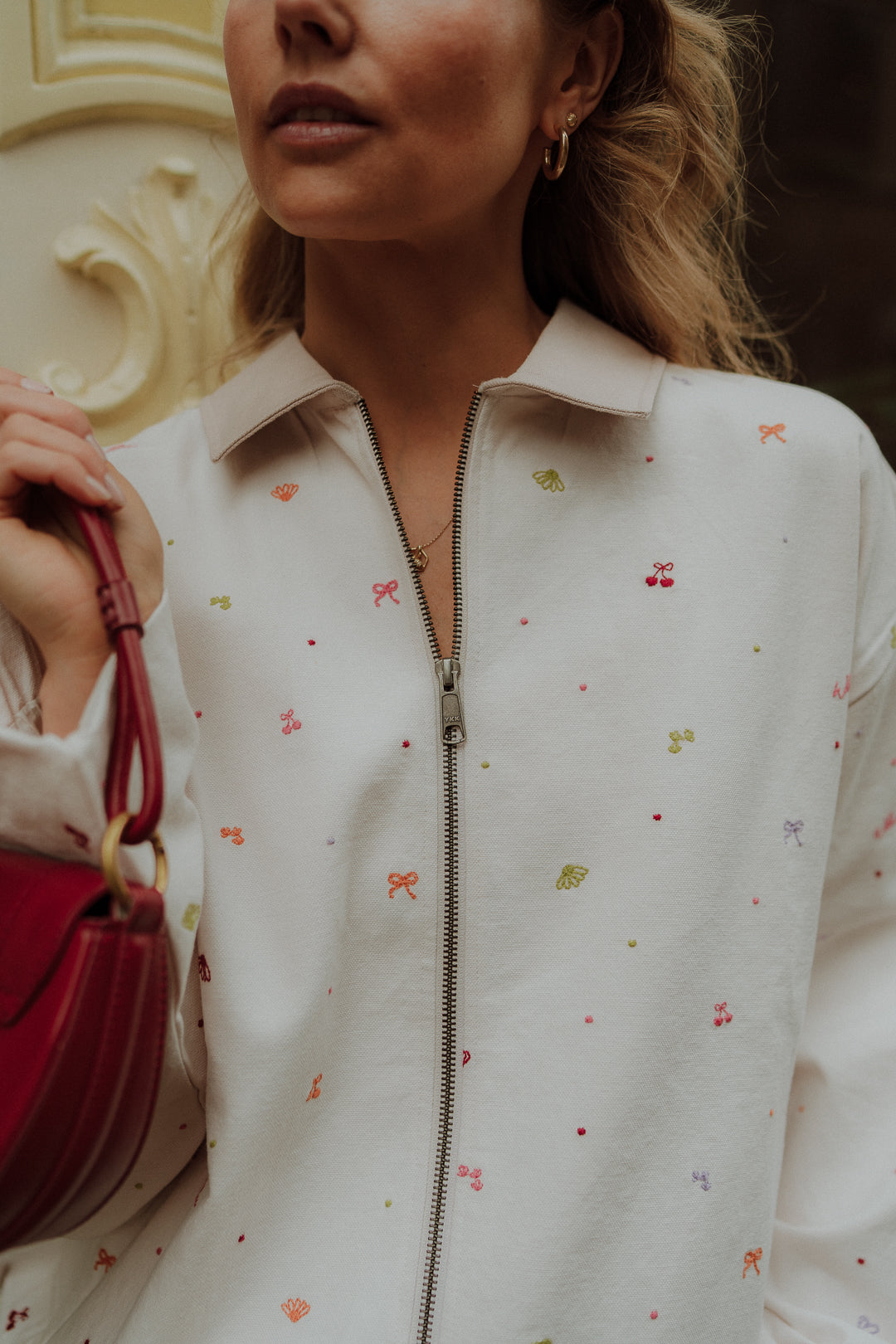 Woman wearing cream zip up jacket with colorful embroidered details