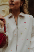Woman wearing cream zip up jacket with colorful embroidered details
