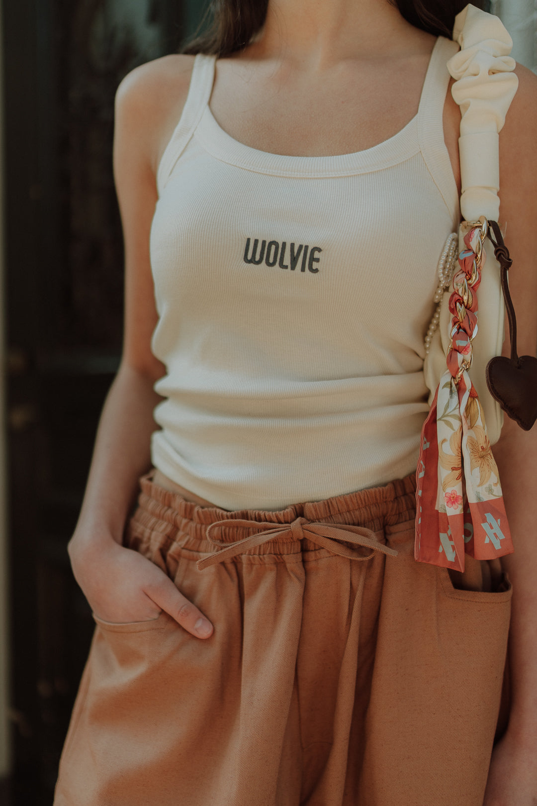 Woman wearing a white ribbed top with wide leg pants and shoulder bag