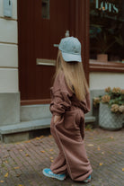 Girl in a mauve oversized tracksuit and blue cap walking outdoors viewed from the back.