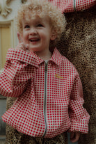 Smiling child wearing a red gingham zip jacket and leopard print pants