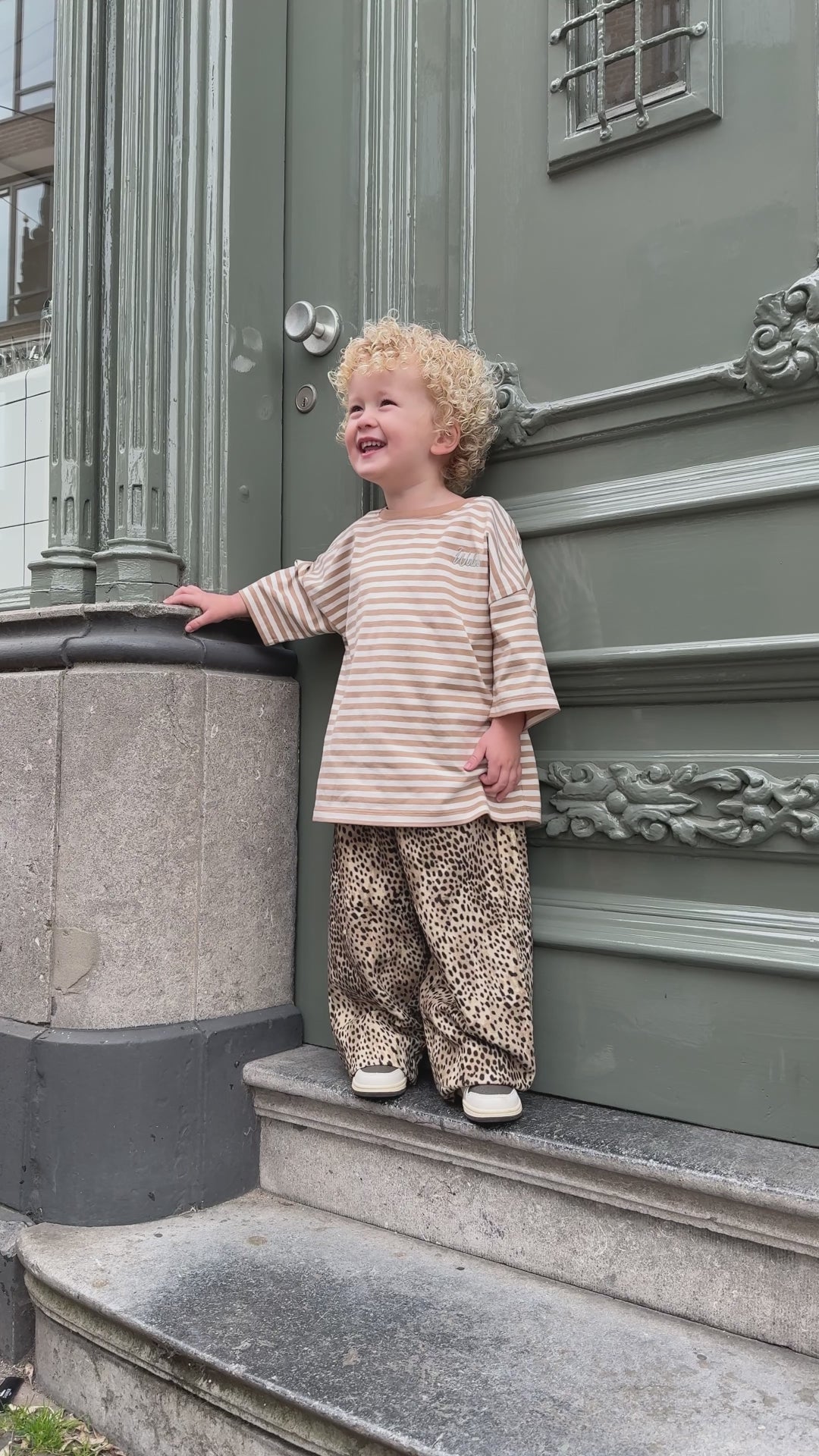 Curly-haired child wearing leopard print pants and a striped oversized shirt in a trendy boys outfit outdoors